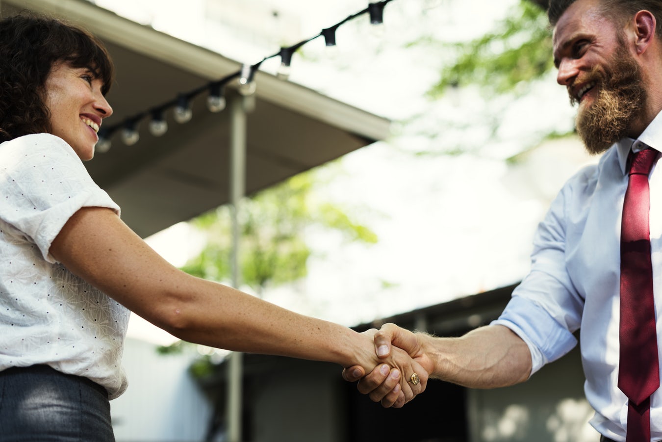 Two business-looking people smiling at eatchother while shaking hands.